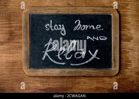 Concetto del periodo di isolamento di quarantena di rimanere a casa. Lavagna vintage con scritte in gesso scritte a mano per rimanere a casa e rilassarsi. Sfondo in legno Foto Stock