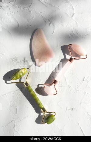Rulli in giada rosa e verde e gua sha per massaggiatori viso. Strumento di bellezza alla moda. Anti-invecchiamento e sollevamento a casa. Composizione minima Foto Stock