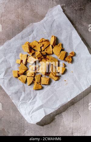 Pokey hokey a nido d'ape o tofee di cenere o caramelle di zucchero coreane di dalgona su carta da forno su fondo grigio di cemento. Piatto, spazio Foto Stock