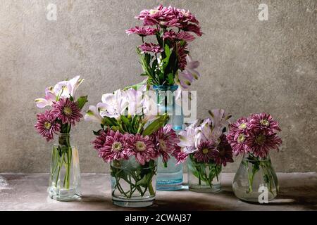 Gruppo di bottiglie e vasi di vetro con bouquet di fiori decorativi rosa su fondo grigio. Foto Stock