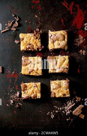 Trend Baking Brookies cioccolato brownie e biscotti torta fatta in casa tagliata da piazze in fila, cioccolato tritato su sfondo nero. Piatto, spazio Foto Stock