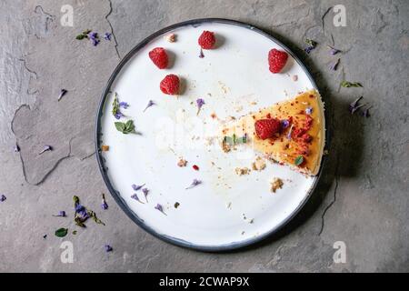 Ultimo pezzo di lampone cotto in casa cheesecake su piatto decorato da lamponi freschi e menta su sfondo grigio textute. Piatto, spazio Foto Stock