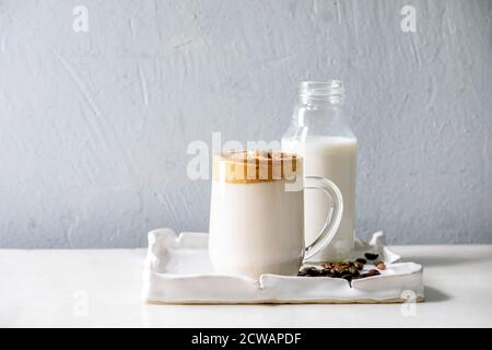 Dalgona Frothy Coffee trend bevanda coreana latte latte latte con schiuma di caffè in tazza di vetro su vassoio in ceramica con ingredienti su tavolo di marmo bianco. Foto Stock