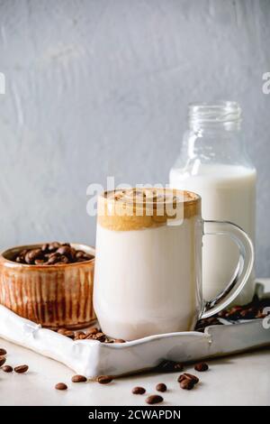 Dalgona Frothy Coffee trend bevanda coreana latte latte latte con schiuma di caffè in tazza di vetro su vassoio in ceramica con ingredienti su tavolo di marmo bianco. Foto Stock