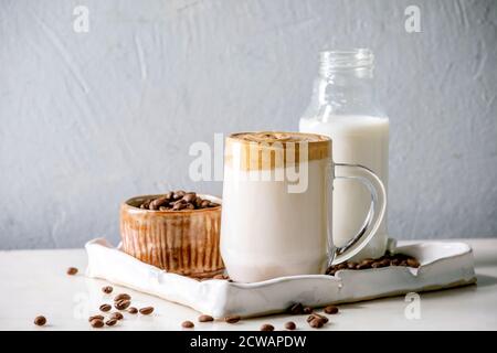 Dalgona Frothy Coffee trend bevanda coreana latte latte latte con schiuma di caffè in tazza di vetro su vassoio in ceramica con ingredienti su tavolo di marmo bianco. Foto Stock