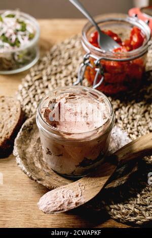 Vasetto di vetro di pate di fegato di pollo fatto in casa con pane di segale a fette, pomodori secchi e insalata di germogli verdi su tavolo da cucina in legno. Colazione a domicilio o a. Foto Stock