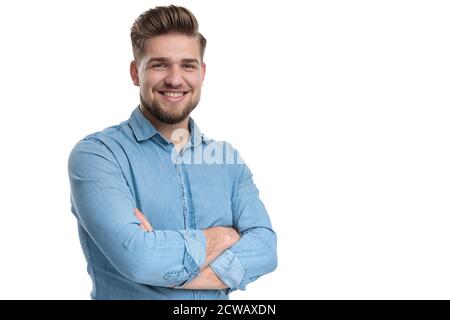 Felice uomo casual sorridente e tenendo la mano attraversata al petto, in piedi su sfondo bianco studio Foto Stock