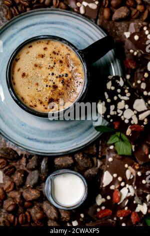 Tazza di caffè espresso con caraffa di latte, cioccolato fondente fatto a mano, caffè e chicchi di cacao intorno a piastrelle di ceramica scura come sfondo. Posa piatta, copia s Foto Stock