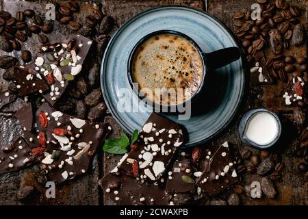 Tazza di caffè espresso con caraffa di latte, cioccolato fondente fatto a mano, caffè e chicchi di cacao intorno a piastrelle di ceramica scura come sfondo. Posa piatta, copia s Foto Stock