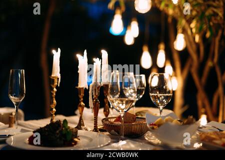 Cena romantica la sera a lume di candela con bicchieri e insalate sui piatti. Foto Stock