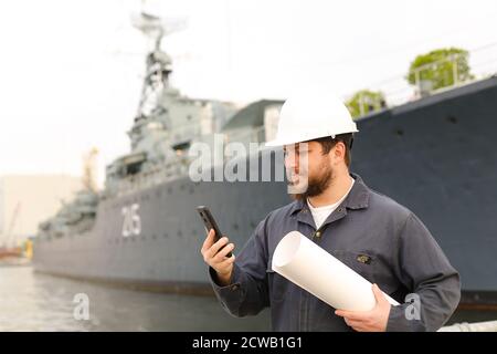 Ingegnere marino che parla da VHF walkie talkie, tenendo carte vicino nave in background. Foto Stock