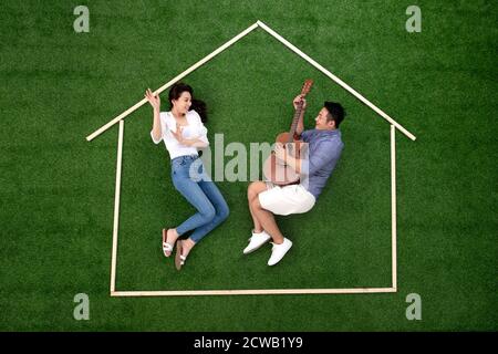 Giovani coppie che si stendono sul profilo della casa d'erba nel canto e ballare Foto Stock