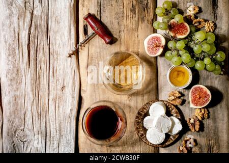 Bicchieri di vino rosso e bianco con uve, fichi, formaggio di capra e noci su vecchio sfondo ligneo. Disposizione piatta, spazio di copia Foto Stock