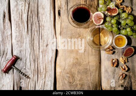 Bicchieri di vino rosso e bianco con uve, fichi, formaggio di capra e noci su vecchio sfondo ligneo. Disposizione piatta, spazio di copia Foto Stock