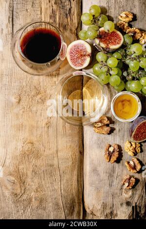Bicchieri di vino rosso e bianco con uve, fichi, formaggio di capra e noci su vecchio sfondo ligneo. Disposizione piatta, spazio di copia Foto Stock