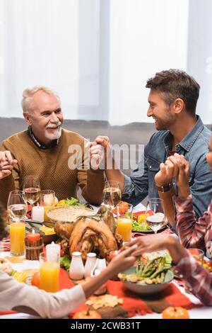 felice famiglia multiculturale che tiene le mani durante la cena in festa di ringraziamento Foto Stock