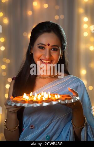 Donna che tiene in mano un piatto pieno di diya e sorridendo Foto Stock