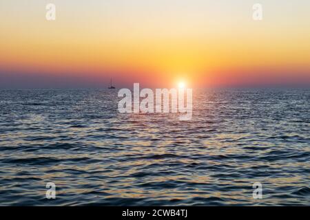 Barca a vela silhouette contro un colorato cielo arancione tramonto in mare aperto Foto Stock