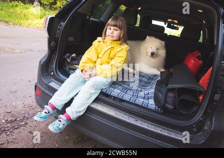 Bambina e cane Samoyed seduto in un tronco di auto della famiglia suv Foto Stock