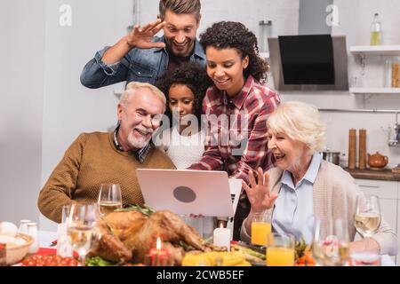 Focalizzazione selettiva della famiglia multiculturale che ha videochiamata sul laptop vicino al cibo durante il ringraziamento Foto Stock