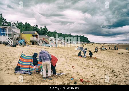 Paesaggio panoramico delle ampie spiagge di Holkham, nel nord di Norfolk, Inghilterra, con capanne e famiglie sotto un cielo tempestoso Foto Stock