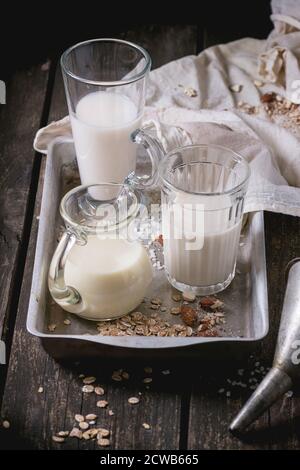 Set di non-latte (latte di riso, latte di mandorla e Latte di avena) in bicchieri di vetro e la brocca sulla vecchia vaschetta di alluminio con grani di riso, fiocchi di avena e mandorla oltre ol Foto Stock