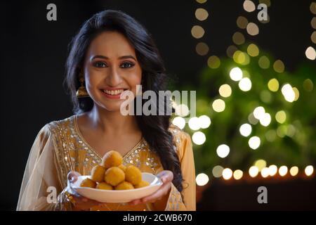 Donna in abbigliamento etnico sorridente con un piatto pieno di ladoos in mano Foto Stock