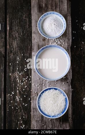 Stile cinese ciotole con latte di riso, farina di riso e riso imbevuto su un vecchio sfondo di legno con grani di riso di cui sopra. Vista dall'alto. Foto Stock