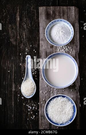 Stile cinese ciotole con latte di riso, farina di riso e riso imbevuto su un vecchio sfondo di legno con grani di riso di cui sopra. Vista dall'alto. Foto Stock