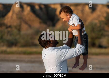 Felice padre afroamericano e figlio che si è bene tempo all'aperto. Il padre che ha divertimento getta in su nell'aria il suo bambino. Concetto di giorno del padre felice. Foto Stock