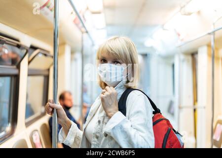 Ritratto di bella donna adulta in maschera medica protettiva con lo zaino si trova in metropolitana e guarda la fotocamera Foto Stock