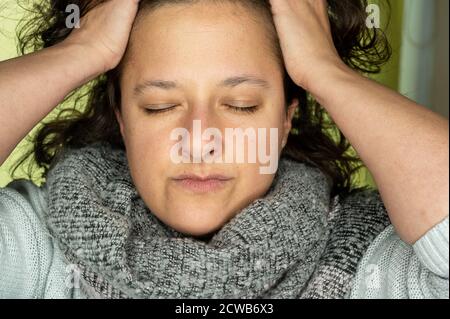 Una giovane donna con gli occhi chiusi afferra i capelli con entrambe le mani. Foto Stock