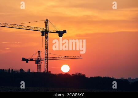 Attività di costruzione sul sito di costruzione. Sagome di gru contro il sole. Foto Stock