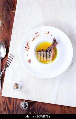 Piatto di ceramica bianca con agnello grigliato ben fatto tritare in brodo giallo con flackes di peperoncino su tavola di marmo bianco su tavolo di legno. Con vinta Foto Stock