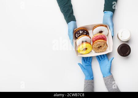 Pausa caffè per pranzo durante la pandemia del covid-19. Cliente in guanti di gomma prende una scatola di ciambelle smaltate e due tazze di caffè Foto Stock