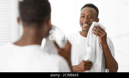 Guy africano Wiping viso con morbido asciugamano in piedi in bagno Foto Stock