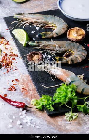 Ingredienti per zuppa tailandese piccante Tom Yam latte di cocco, peperoncini, funghi shiitake e gamberi su lavagna nera su sfondo di pietra. Foto Stock