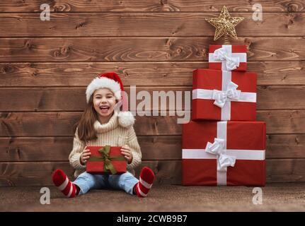 Buon Natale e buon Natale concetto. Carino bambina con regali di natale su sfondo di legno. Ritratto di bel bambino a Santa Hat wi Foto Stock