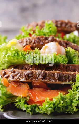 Set di panini con pane integrale, insalata fresca, formaggio feta, pomodori ciliegini, gamberi e salmone salato su piatto di metallo vintage su legno bianco Foto Stock