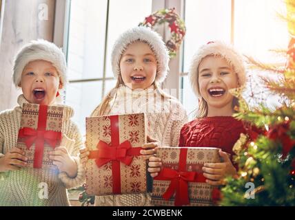 Buon Natale e buone feste! Allegri e simpatici regali di apertura per i bambini. I bambini si divertono vicino all'albero al mattino. Famiglia amorevole con regali in roo Foto Stock