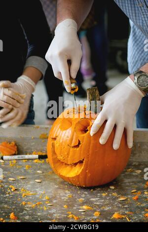 Processo di fabbricazione di zucche di Halloween. Le mani nei guanti di gomma a fette la zucca da piccoli seghetto. Foto Stock