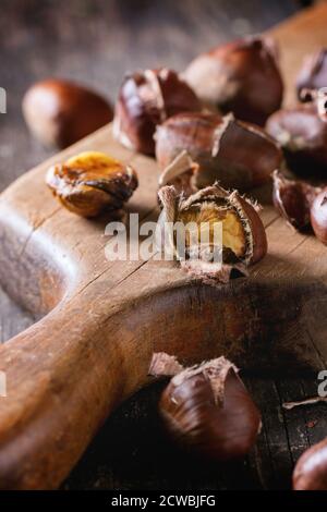 Primo piano di castagne commestibili alla griglia sbucciate e non sbucciate tagliere d'epoca sopra il vecchio tavolo di legno Foto Stock