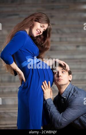 Bell'uomo ascolta la pancia della sua bella moglie incinta e sorrisi Foto Stock