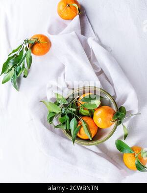 Vaso in ceramica di mandarini con foglie di colore bianco sulla superficie tessile. Vista superiore Foto Stock