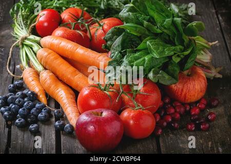 Assortimento di frutta fresca, verdura e bacche di carote, spinaci, i pomodori, le mele rosse, mirtilli e mirtilli rossi sopra il vecchio tavolo in legno. Foto Stock