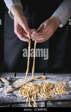 Mani femminili pasta pici in legno tavolo da cucina, polverizzazione da farina. Scuro in stile rustico. Foto Stock