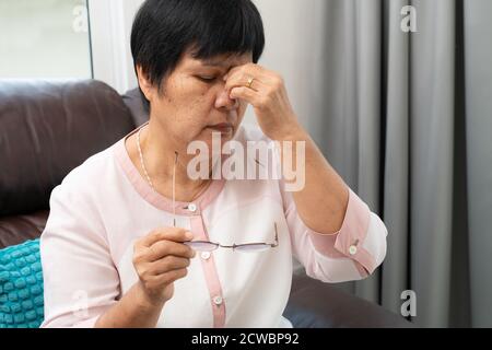Vecchia donna rimozione degli occhiali, massaggiare gli occhi dopo aver letto il libro cartaceo. provare disagio a causa di lunghi indossando occhiali, affetti da occhi Foto Stock