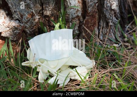 Una maschera medica di protezione e guanti chirurgici sono stati utilizzati persi sul terreno erboso. Maschera monouso in natura. Scartare in modo errato la fa utilizzata Foto Stock