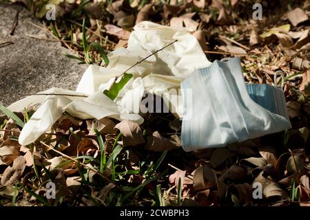 Una maschera medica di protezione e guanti chirurgici sono stati utilizzati persi sul terreno erboso. Maschera monouso in natura. Scartare in modo errato la fa utilizzata Foto Stock