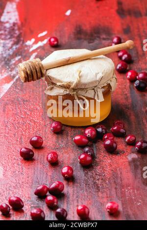 Vasetto di vetro di miele liquido con nido d'ape all'interno, e mirtilli freschi su tavola di legno rosso e nero. Foto Stock